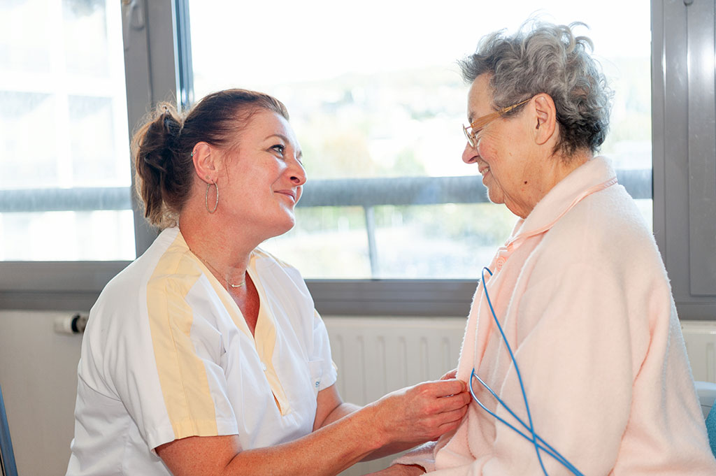 Une aide-soignante et une patiente âgée sont dans une chambre et se regardent affectueusement